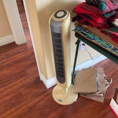 Sale Photo Thumbnail #102: Holmes cream-colored oscillating tower fan standing next to a folding table laden with folded linens.