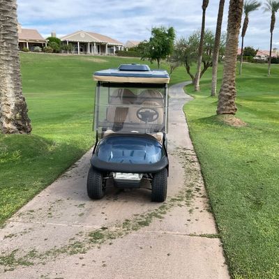 Sale Photo Thumbnail #3: Blue golf cart with clear windshield and overhead canopy, parked on a concrete path within a golf course community.