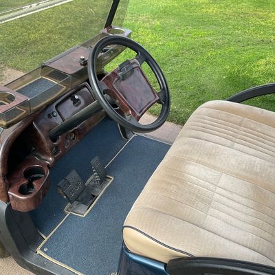 Sale Photo Thumbnail #8: Interior view of a custom golf cart featuring a woodgrain-style dash, beige fabric upholstery, blue carpeting, and dual cupholders.