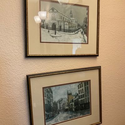 Sale Photo Thumbnail #163: Pair of framed art prints depicting European streetscapes, matted under glass in matching dark wood frames with gold trim.