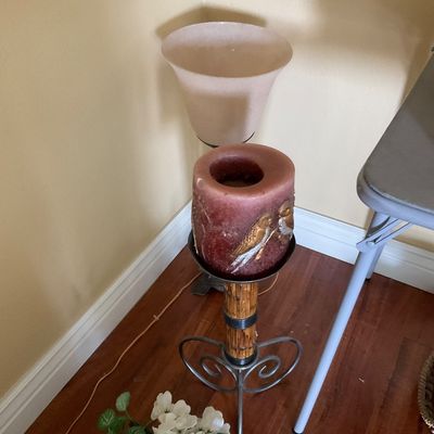 Sale Photo Thumbnail #86: Large decorative pillar candle featuring painted bird accents on a metal and bamboo-style stand, displayed alongside a floor torchere lamp.