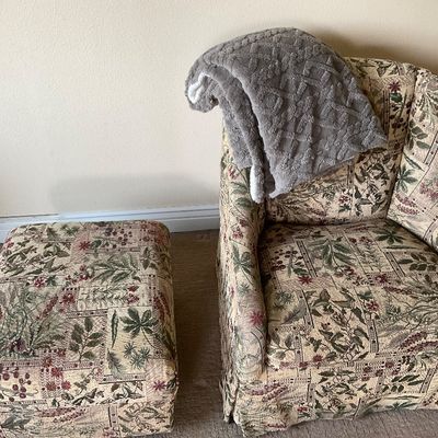 Sale Photo Thumbnail #153: Traditional upholstered armchair and matching ottoman with a botanical tapestry fabric pattern, paired with a plush gray throw blanket.