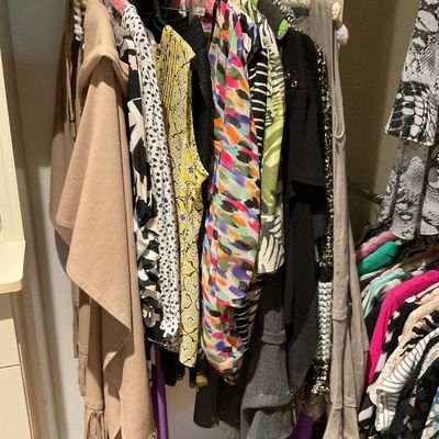 Sale Photo Thumbnail #169: A collection of women's clothing hanging in a closet, including a tan fringed poncho, patterned tops, and colorful dresses.