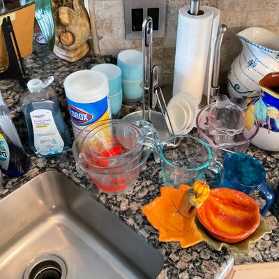 Sale Photo Thumbnail #105: Collection of assorted kitchen items, including glass measuring cups, decorative ceramic pitchers, cleaning supplies, and autumn-themed trinket dishes displayed on a granite countertop.