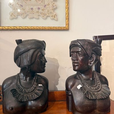 Pair of vintage hand-carved dark wood busts depicting a male and female figure, featuring intricate headdresses and collar necklaces.