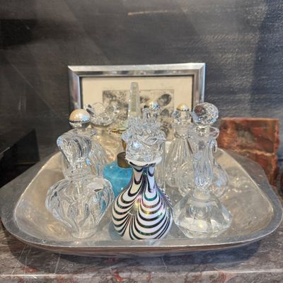 Collection of vintage glass perfume bottles arranged on a silver-tone vanity tray, including cut crystal and art glass pieces with...