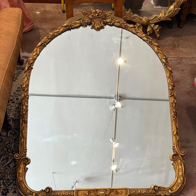 Large French-style wall mirror featuring a giltwood arched frame with floral cresting and scrolling corner accents.