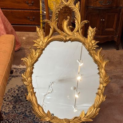 Ornate French Rococo-style giltwood oval wall mirror featuring an elaborate acanthus leaf frame and cresting.