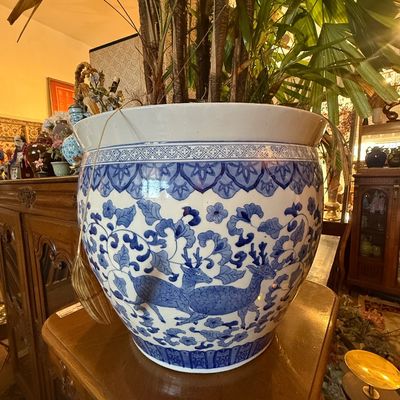 Large Chinese blue and white porcelain fish bowl planter featuring deer, floral, and vine motifs, housing a potted palm plant.