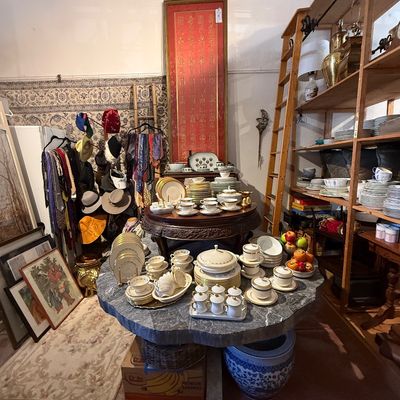 An extensive collection of porcelain dinnerware and teacups displayed on tables alongside Asian decorative art, framed wall hangings, and...