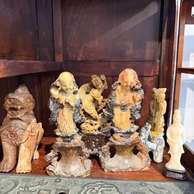 Collection of carved Asian soapstone and wooden figurines, including luohan or immortal figures and a foo dog, displayed inside a wooden...