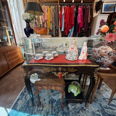 Ornate French-style black and gold lacquered writing desk with red leather top, displayed alongside Asian porcelain tea sets, figurines,...