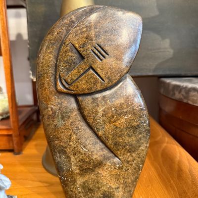 Hand-carved stone sculpture featuring an abstract, stylized figure with minimalist facial details in a Shona style.