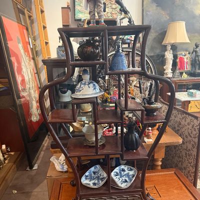Vintage Asian-style dark wood curio display shelf holding small porcelain collectibles, featuring an asymmetrical multi-tiered design and...