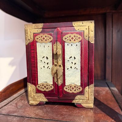 Vintage Asian-style red wooden jewelry cabinet featuring ornate brass hardware and carved jade-colored stone panel inserts on the double...