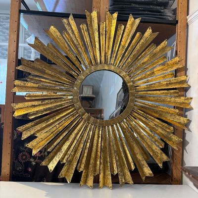 Mid-century modern sunburst wall mirror featuring a distressed gilt finish with layered, folded-metal rays.