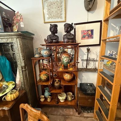 Collection of home decor items featuring an antique carved wooden tiered shelf displaying floral art pottery, flanked by pair of dark...