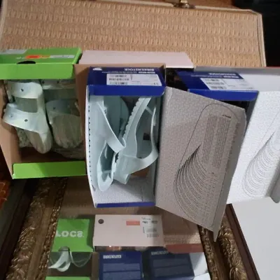 Selection of light blue and white sandals, including Birkenstock and Crocs, displayed in their original shoe boxes.