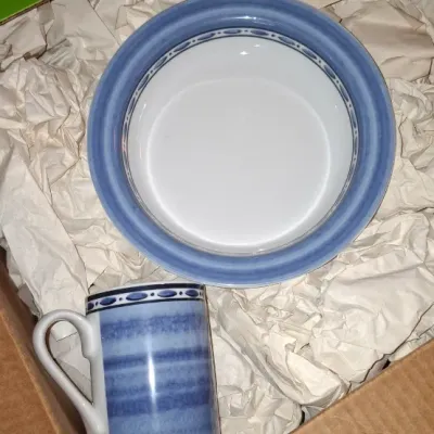 Sale Photo Thumbnail #221: Ceramic bowl and matching mug with blue striped pattern packed in paper inside a cardboard box.