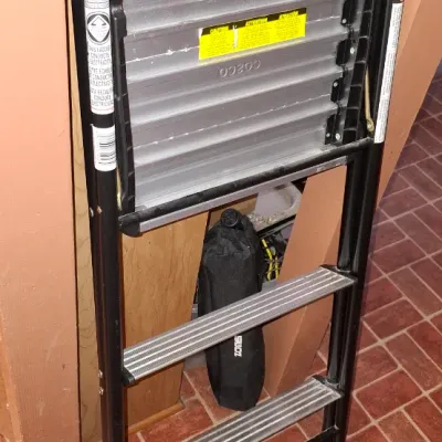 Black metallic step ladder with aluminum treads and top platform tray, showing typical light wear from use.