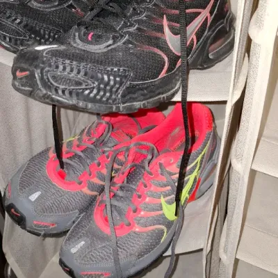Two pairs of Nike athletic shoes stored on a fabric hanging organizer shelf, including a black pair with hot pink accents and a gray pair...