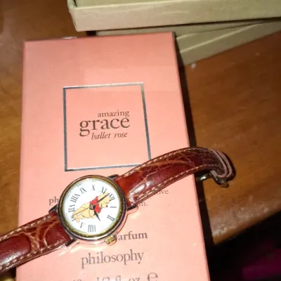 Sale Photo Thumbnail #140: Novelty Winnie the Pooh wristwatch with brown leather strap resting on a boxed bottle of Philosophy Amazing Grace Ballet Rose perfume.