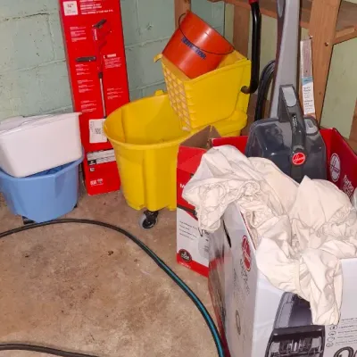 Sale Photo Thumbnail #157: Collection of household cleaning supplies including a yellow commercial mop bucket on casters, a Hoover carpet cleaner with its original box, and plastic storage tubs.