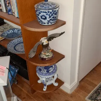 Sale Photo Thumbnail #261: Corner shelving unit displaying blue and white porcelain items, a bald eagle figurine, books, and home decor.