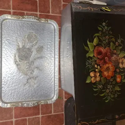 Two vintage serving trays, including a hand-hammered aluminum tray with embossed floral details and a black lacquered metal tray...