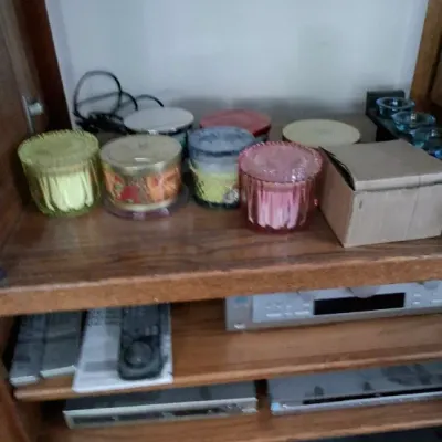 Sale Photo Thumbnail #250: Collection of decorative jar candles displayed on the upper shelf of a wooden entertainment cabinet alongside various home audio-visual components.