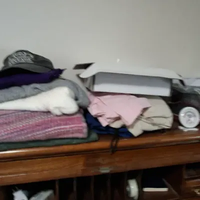 Sale Photo Thumbnail #111: Assortment of folded clothing items, a baseball cap, and boxed goods stacked atop a wooden roll-top desk.