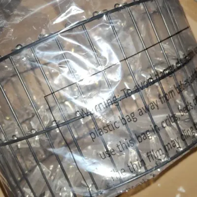 Black metal wire chandelier frame wrapped in protective plastic packaging, resting inside a cardboard box.