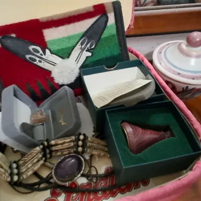 Sale Photo Thumbnail #148: Collection of Southwestern and Native American style jewelry and collectibles, featuring bone hairpipe necklaces, boxed items, and a fabric pouch, displayed inside a pink fabric case.