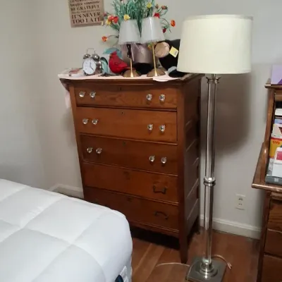 Sale Photo Thumbnail #114: Vintage tall wooden dresser with glass knobs alongside a contemporary brushed nickel floor lamp.