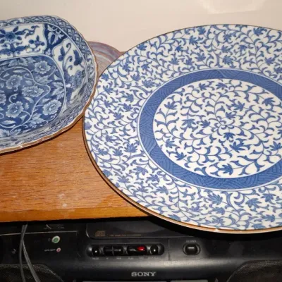 Sale Photo Thumbnail #262: Two blue and white porcelain plates with intricate floral scroll designs, displayed on a wooden shelf above a Sony cassette player.