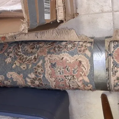 Sale Photo Thumbnail #210: Rolled Persian-style area rug featuring blue, pink, and cream ornate floral patterns with fringe edges, taped for storage.