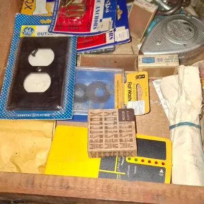 Sale Photo Thumbnail #158: Wooden workshop drawer filled with assorted vintage hardware, including a General Electric outlet cover, boxed wire connectors, plastic anchors, and small tools.