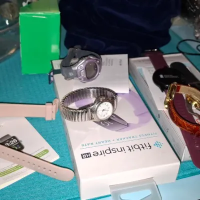 Collection of modern wristwatches and fitness trackers, including a Fitbit Inspire HR in original box, a rose gold smartwatch, and...
