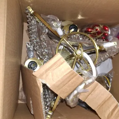 Box filled with disassembled brass and crystal light fixture parts and holiday decorations.