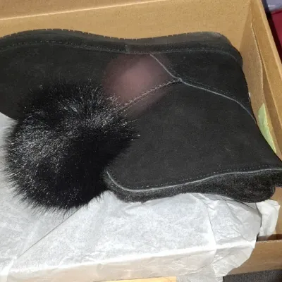Sale Photo Thumbnail #282: Black suede ankle boot featuring a black faux fur pom-pom detail, resting inside its original shoe box with tissue paper.