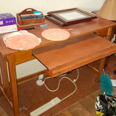 Wooden computer desk with a pull-out keyboard tray, holding miscellaneous items including decorative plates, picture frames, and a desk...