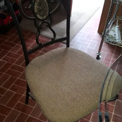 Contemporary metal dining chair featuring a decorative scrollwork backrest with a central stone insert and a beige textured fabric padded...