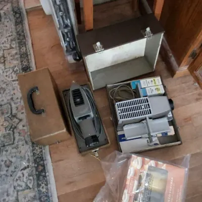 Sale Photo Thumbnail #245: Vintage slide projector and portable power tools with carrying cases sitting on a hardwood floor next to a runner rug.