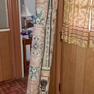Two rolled area rugs leaning against a wall, including one brand-new washable rug in factory plastic packaging featuring a floral pattern.