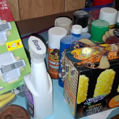 Assortment of household cleaning supplies and hardware, including Command broom grippers, Bona spray, Gorilla foam sealant, and a box of...