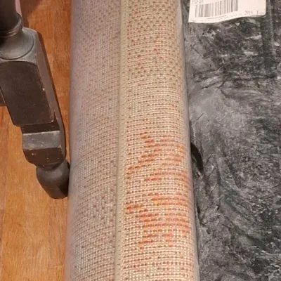 Sale Photo Thumbnail #255: Rolled woven area rug featuring neutral tones with rust-orange geometric accents, stored alongside a packaged carpet pad.