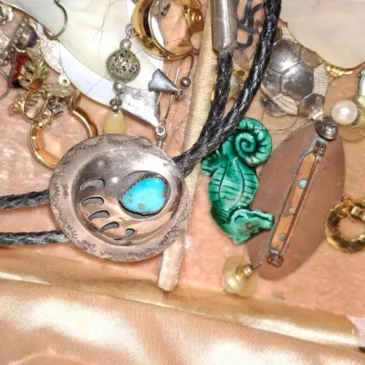 Sale Photo Thumbnail #144: Collection of assorted vintage jewelry inside a pink velvet-lined jewelry box, featuring a Native American style sterling silver and turquoise bear paw bolo tie, carved seahorse charm, and gold-tone earrings.