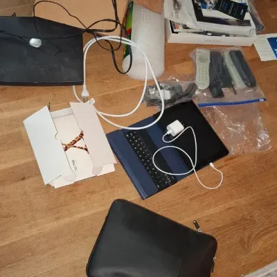 Sale Photo Thumbnail #260: Collection of assorted modern electronics, including a tablet with a keyboard case, black computer sleeve, remotes, cables, software packaging, and a Dreo water filter box.