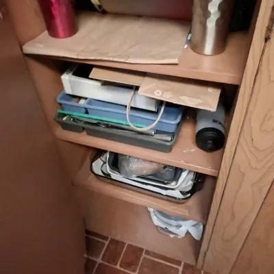 Open kitchen cabinet filled with various items, including insulated water bottles, travel mugs, organizer trays, and baking pans.