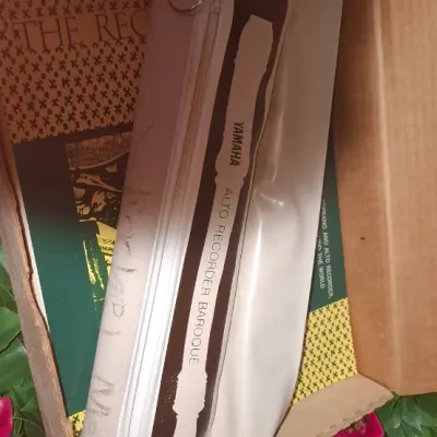 Yamaha Baroque alto recorder in its original cream and brown zippered case, accompanied by a music book, stored inside a cardboard box.